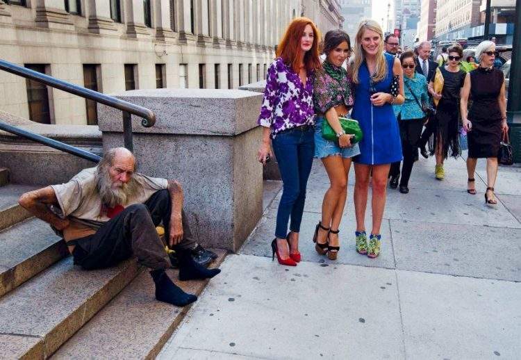 Fashionistas pose for photographs in front of a homeless man outside Moynihan Station following a showing of the Rag & Bone Spring/Summer 2013 collection during New York Fashion Week 1