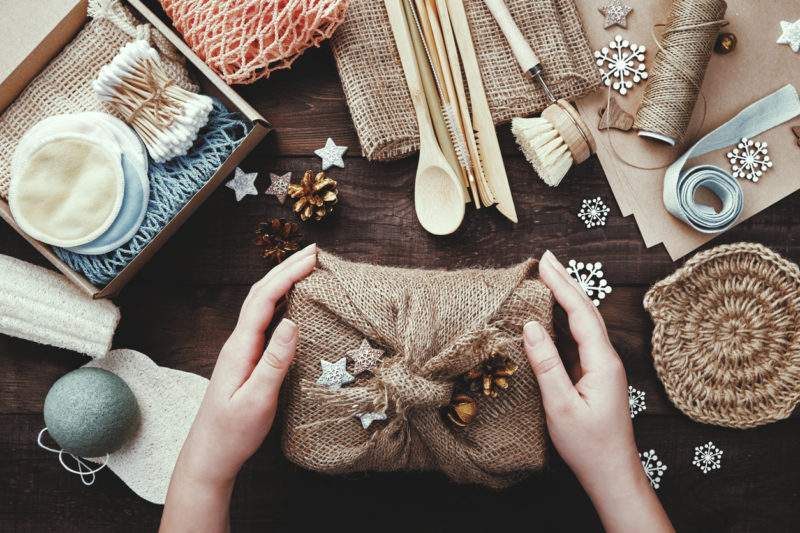 Zero waste christmas. Female hands hold gift wrapped in burlap. Eco friendly products laid out on table 1