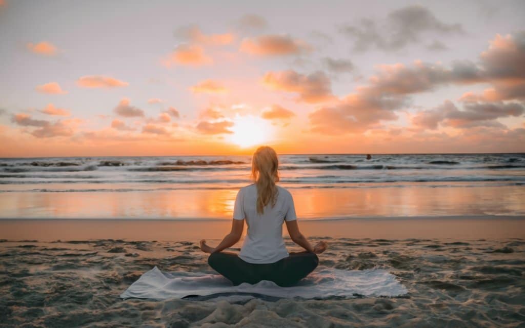  A meditation space on a sunset beach, a contemplative person in lotus position facing the sea, with waves gently breaking on the shore, warm sunlight tinting the sky in orange and pink hues, Photography, DSLR camera, 50mm lens, --ar 16:9 --v 5